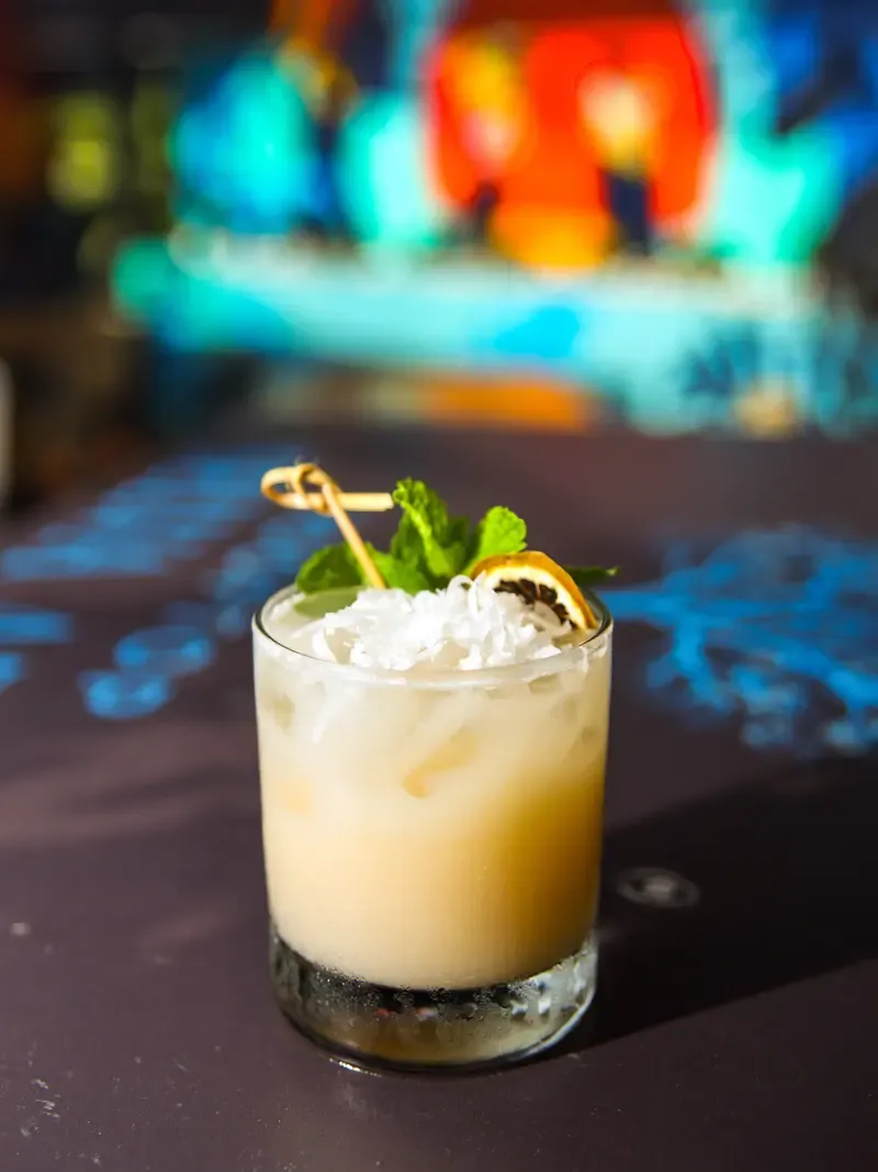 Cóctel cremoso con coco rallado, menta y una rodaja de cítrico deshidratado.