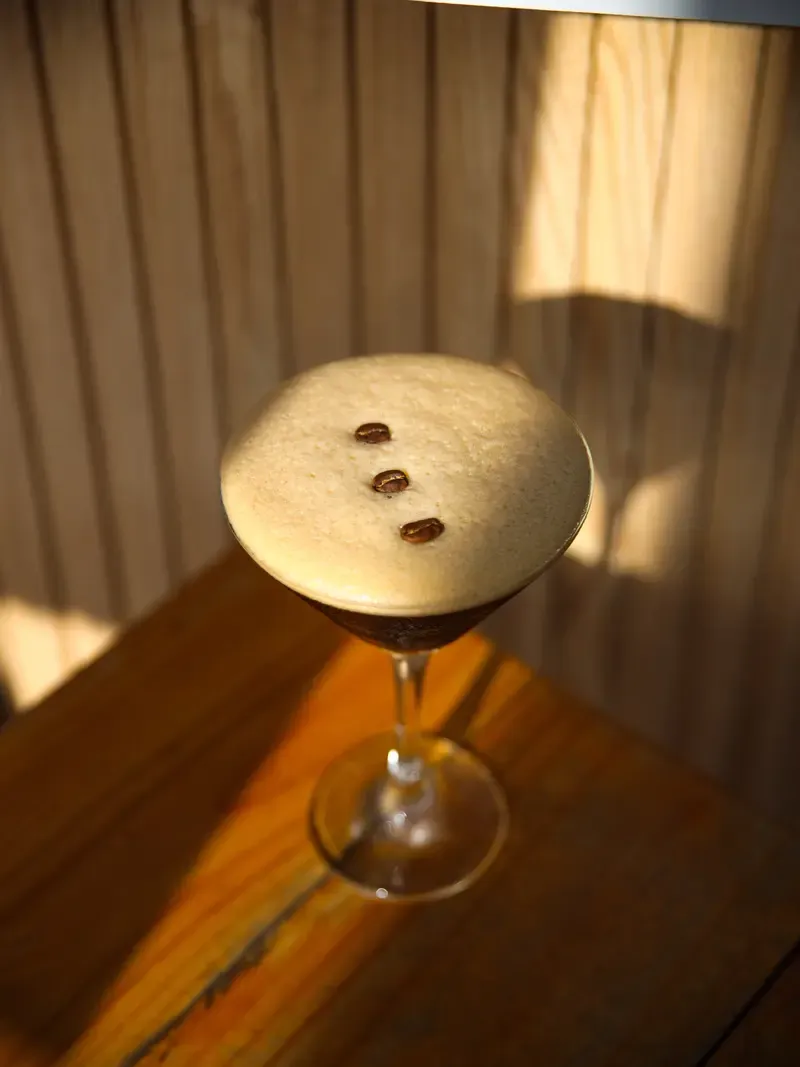Copa de cóctel de café con espuma y tres granos de café encima, sobre una mesa de madera.