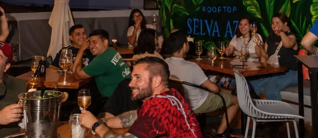 Grupo de amigos riendo en las mesas del rooftop, con el mural de selva detrás.